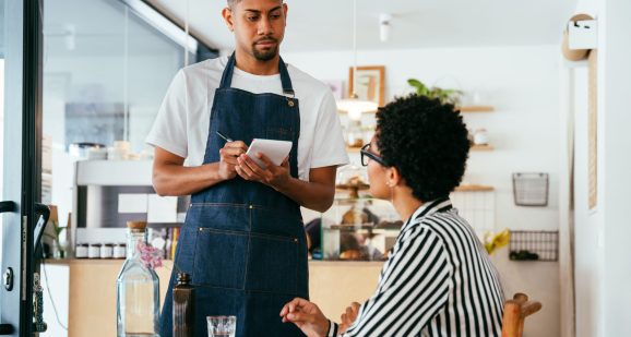 Bakery, happy portrait of hispanic black man in cafe ready for serving pastry, coffee and baked foods. Restaurant, coffee shop and confident waiter barista by counter for service, help and welcome